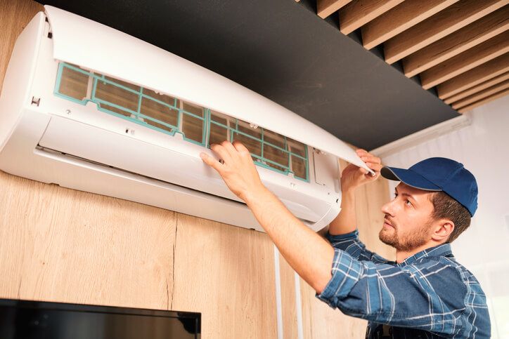 HVAC Specialist performing annual maintenance on ductless heating and cooling ventilation system unit inside a client's home.