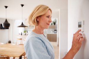 Woman adjusting her digital thermostat inside her home, kitchen and dining room in the background.