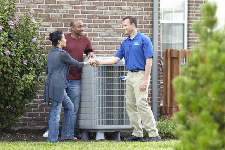 HVAC specialist consulting with a couple outside their home next to their AC system unit.