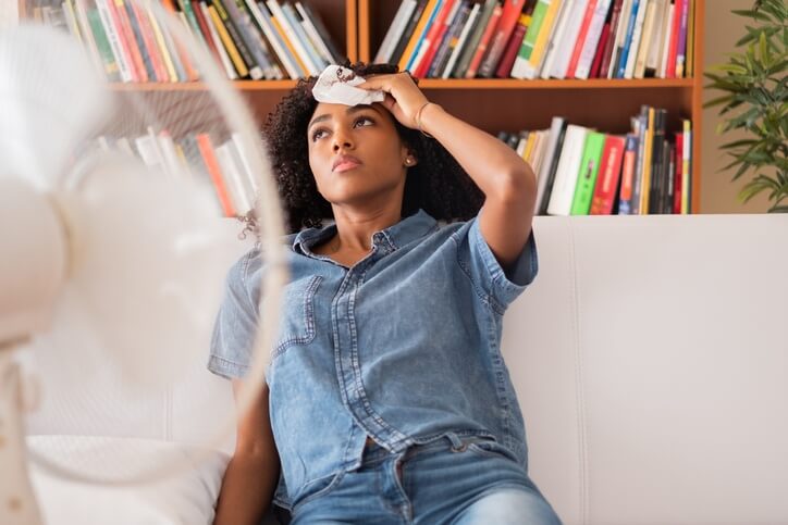 A woman tries to cool off in front of a fan as she dabs her forehead with a tissue.