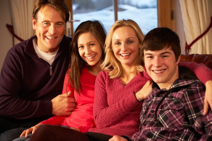 A happy family of four relaxing on the couch in their comfortably heated home.