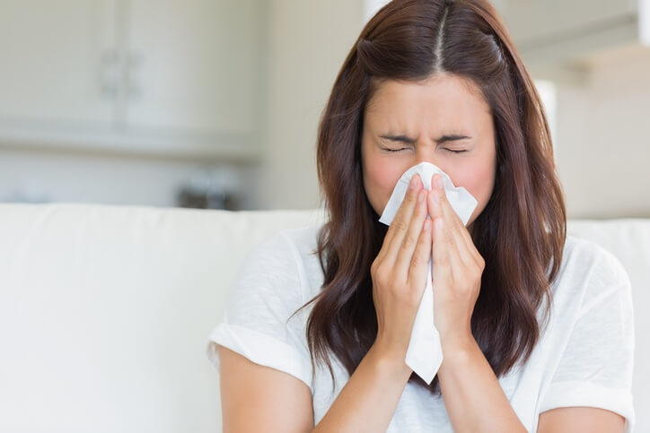 A woman with allergies blowing her nose into a tissue.