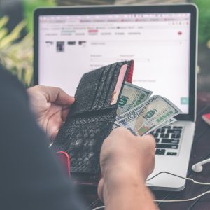 Someone pulling cash out of a wallet in front of a laptop computer, deciding if new AC is in the budget this summer.