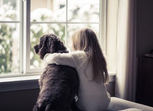 girl in white sweater looks out window with dog