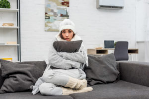 woman sits on couch wrapped in blanket and wearing a winter hat