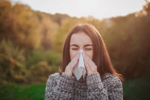 woman sneezing into tissue with fall background